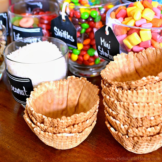 Waffle bowls and other sundae toppings on a wood table.