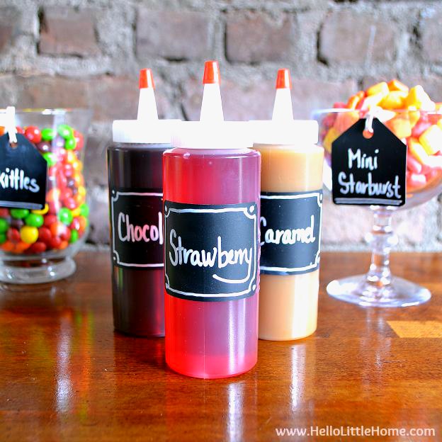 Three syrup bottles with chalkboard labels on a food table.