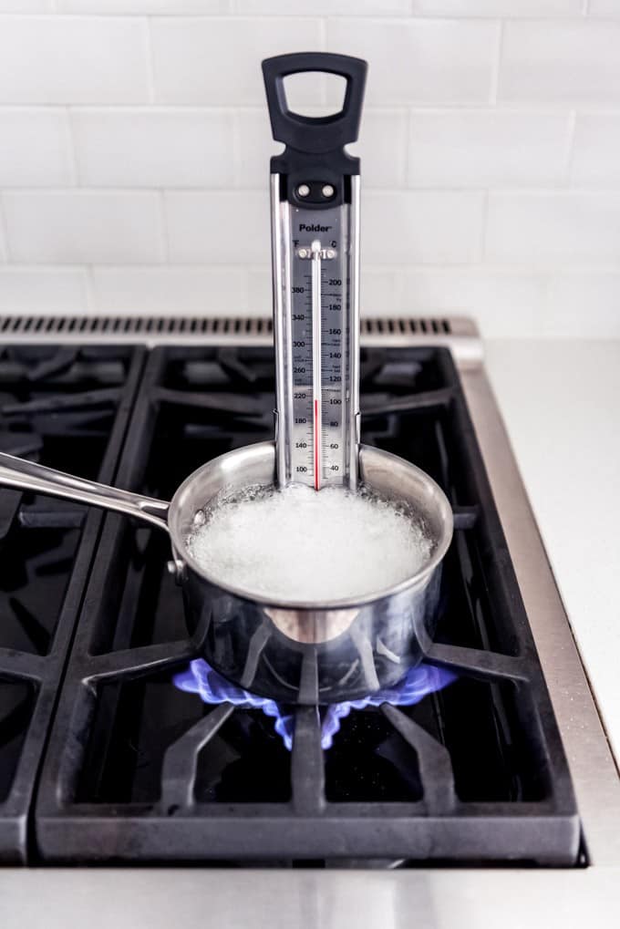 An image of a saucepan with sugar, corn syrup, and water on the stove with a candy thermometer in it.
