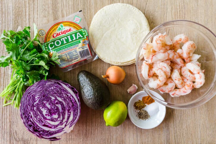 Shrimp Tacos are loaded with shrimp, cabbage, avocado, cotija, cilantro and served over gluten free corn tortillas. The shrimp taco sauce will win you over! Shrimp Taco Ingredients with tortillas, raw shrimp, seasonings in bowl, avocado, cabbage and cotija cheese