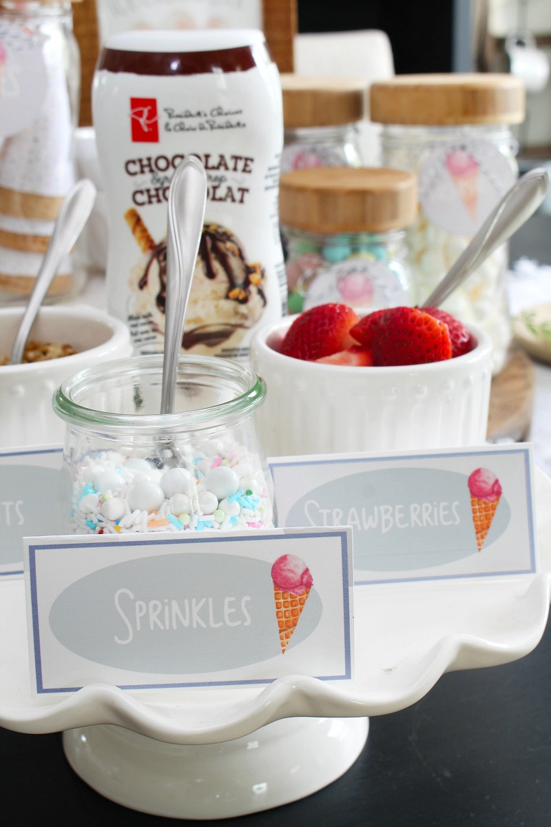 Ice Cream Sundae Bar Printables 45 Ice cream sundae bar with toppings on a cake stand.