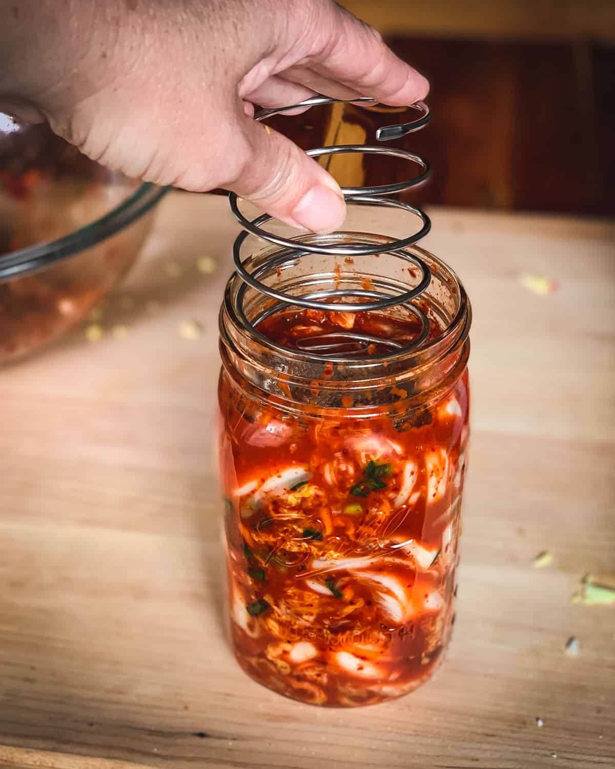 Kimchi is a spicy Korean side dish that is traditionally fermented, similar to sauerkraut. It is usually made with napa cabbage along with other vegetables like carrots, onions, ginger, and garlic. Korean chili flakes give it a spicy kick! Kimchi is surprisingly easy to make and so delicious! putting the fermenting spring into the jar of kimchi