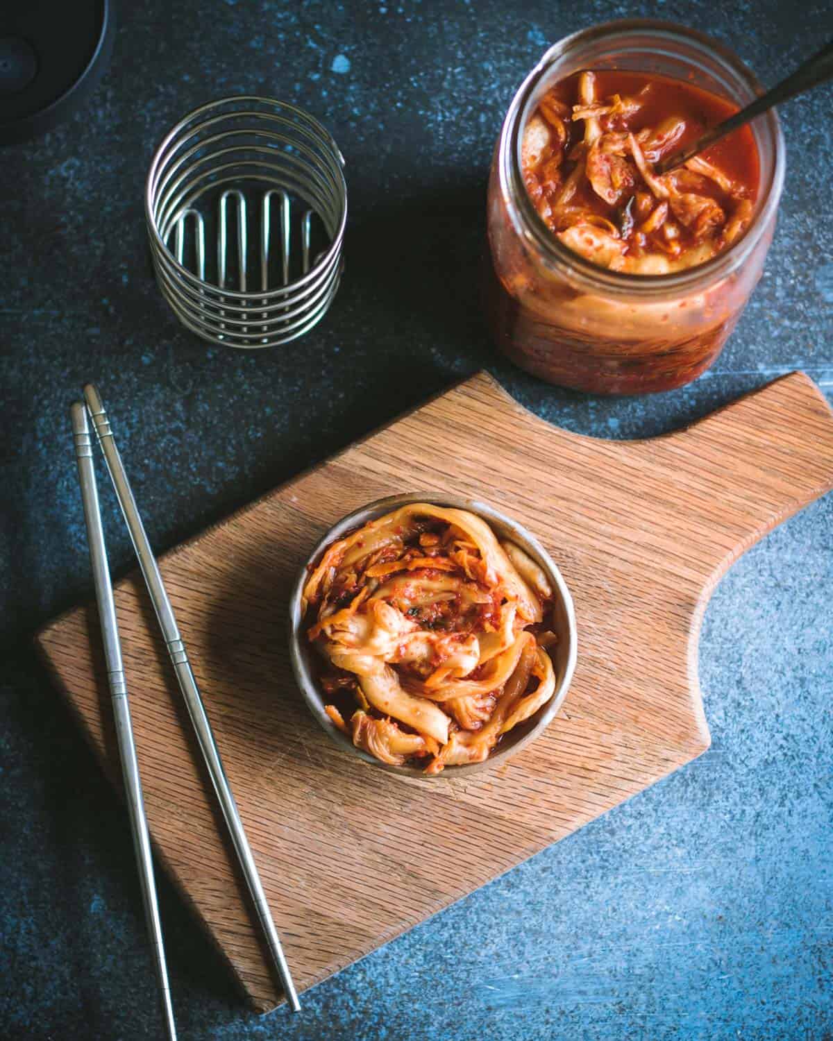 Kimchi is a spicy Korean side dish that is traditionally fermented, similar to sauerkraut. It is usually made with napa cabbage along with other vegetables like carrots, onions, ginger, and garlic. Korean chili flakes give it a spicy kick! Kimchi is surprisingly easy to make and so delicious! a bowl of kimchi with chopsticks