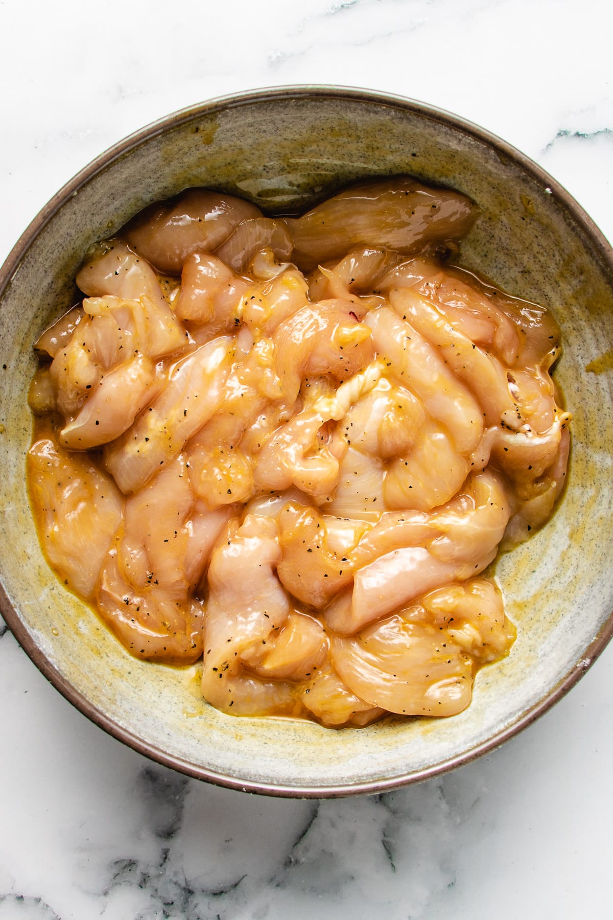 Photo shows thinly sliced chicken breast seasoned with marinade