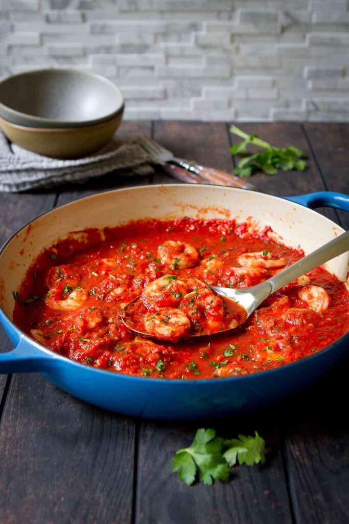 Shrimp in Red Sauce Recipe 17 Italian shrimp dinner in skillet, with bowls in background.