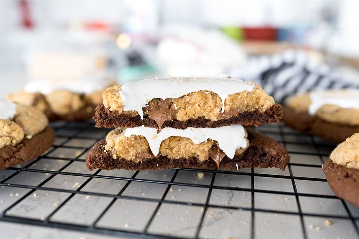 S'mores Brownie Cookie (Crumbl Copycat) - Cooking With Karli 10 cookie broken in half, stacked on top of each other with chocolate and marshmallow oozing.