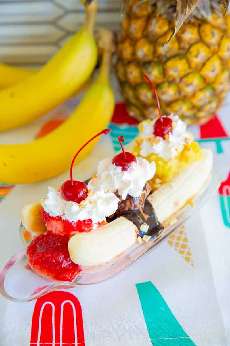 Old-Fashioned Ice Cream Banana Split 13 Ice Cream Banana Split on a banana boat dish, ripe banana and pineapple on background